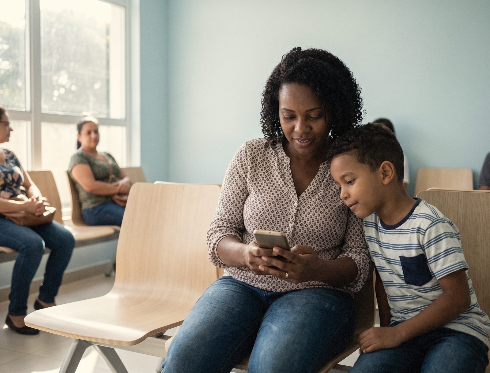 Mãe e filho na sala de espera de uma clínica, olhando o celular